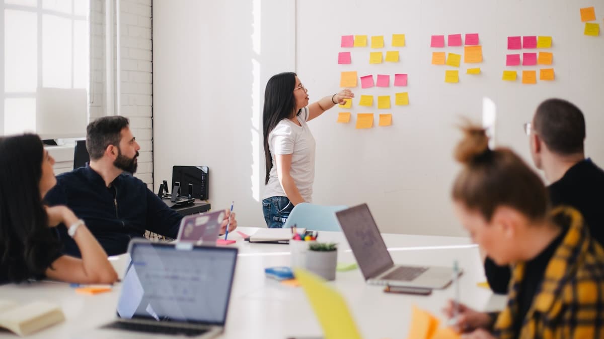 A team collaborating around a table with laptops and sticky notes on a wall