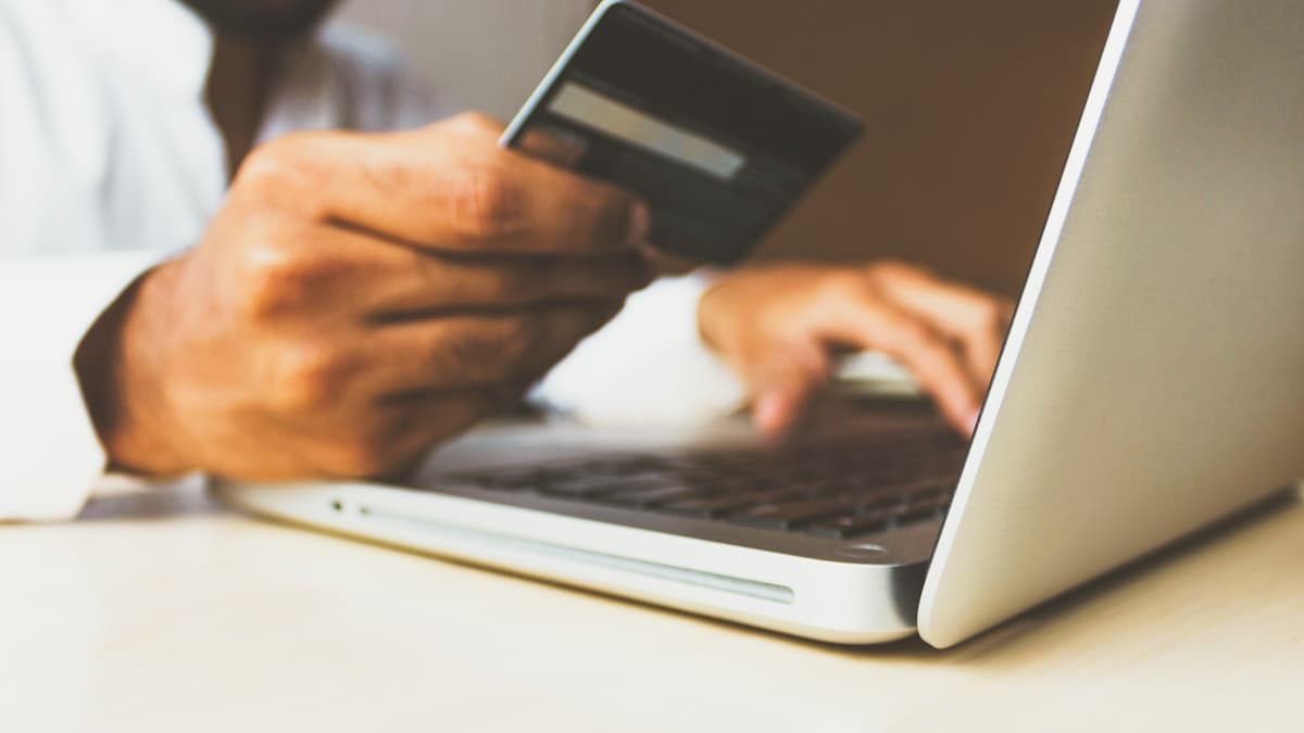 A hand holding a credit card next to a laptop, making an online purchase